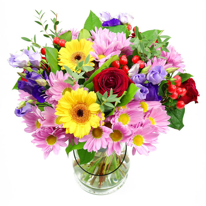 In this image, a generous mixed bouquet stands tall in a cylindrical clear glass vase, the pristine white background making every bloom appear crisp and vivid. At its core, several deep red roses spiral open, their velvety petals layered tightly, bringing classic elegance and depth. Nestled alongside, two bright yellow gerbera daisies with warm brown-orange centres radiate a cheerful, almost sunlit energy, immediately catching the eye. Surrounding these stars is a collar of soft pink and mauve daisies or chrysanthemums, each flower formed from many fine petals around a small yellow centre, creating a cushiony, cloud-like volume. Threaded throughout the design are stems of purple and lavender lisianthus, their bell-shaped blossoms curling gently at the edges, adding cool tones and an air of refined grace, like a quiet corner of a St Luke's café bouquet brought to life. Clusters of shiny red hypericum berries punctuate the arrangement, small and round, adding a tactile contrast to the softness of the petals and a hint of playful detail. A mix of lush green foliage frames the whole piece: broader, darker leaves give structure, while lighter, more delicate sprigs soften the outline and introduce a sense of movement, as though the bouquet has just been set down after a walk from a local St Luke's florist. The stems are visible through the vase, neatly trimmed and resting in clear water, emphasising freshness and professional care. The mood of the arrangement is uplifting and generous, ideal for birthdays, thank-you gestures, or welcoming a new neighbour, bringing a burst of colour and gentle fragrance into any St Luke's home.